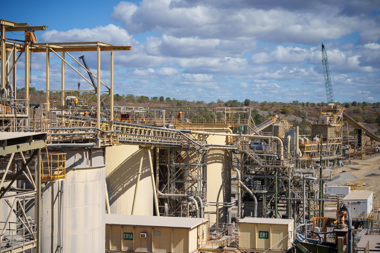 Aerial view of the Ravenswood Gold Mine processing plant infrastructure, Queensland, showing conveyor systems, tanks, and mine facilities under a blue sky