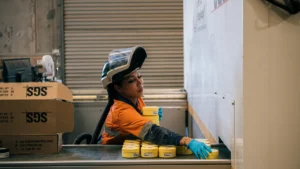 Laboratory technician in orange hi-vis seated beside SGS-branded boxes in a commercial assay facility