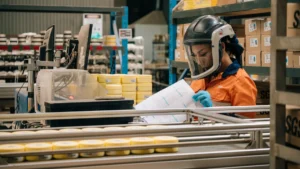 Laboratory technician in orange hi-vis loading sample jars onto a PhotonAssay™ conveyor system in a commercial assay laboratory