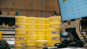 Stacked yellow PhotonAssay™ sample jars with barcoded labels beside a barcode scanner in a laboratory