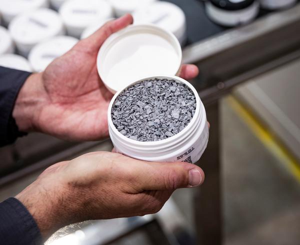 Hands holding an open PhotonAssay™ sample jar filled with crushed ore, ready for analysis