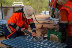 Geologist in hi-vis and hard hat laying drill core into a core tray at a drill site